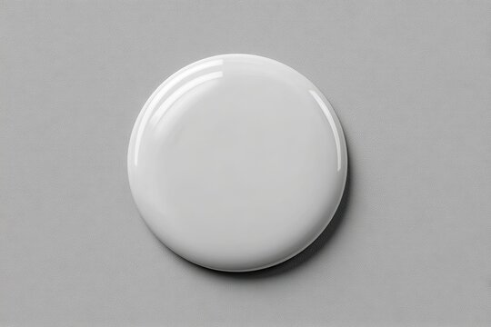 High-angle close-up of a perfectly round, glossy, white liquid droplet or paint blob on a neutral gray surface