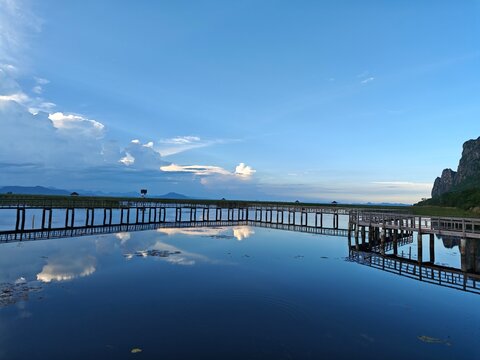 Scenic wooden walkway over calm lake with mountain and sky reflection