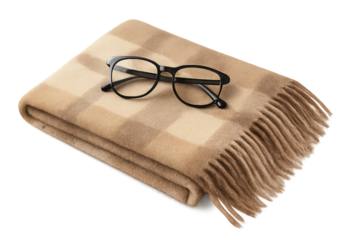 Beige plaid blanket folded with fringe, eyeglasses resting on top