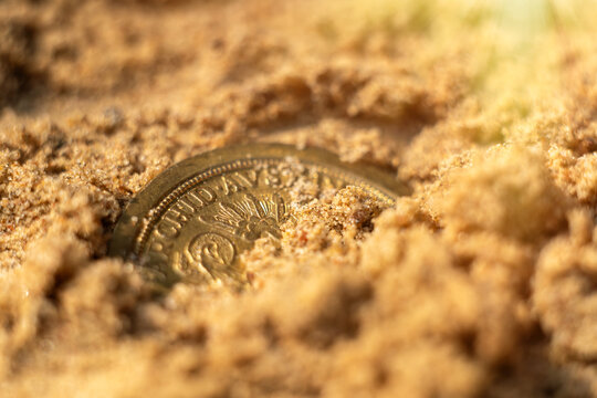 A gold coin in the sand on the beach.Find a treasure trove of coins.Jewelry search.