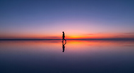 Fototapeta premium Silhouette Stroll Person Reflecting in Waters at Sunrise
