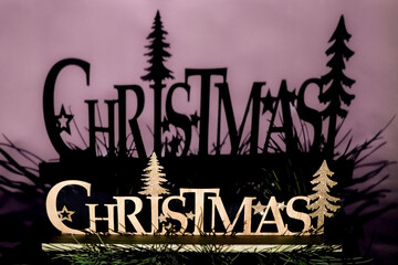 Wooden 'christmas' sign with glitter trees creating a strong shadow against a purple wall,...