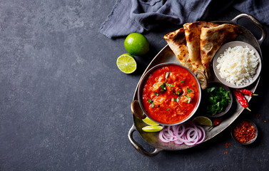 Authentic Indian feast: chicken tikka masala with rice, naan, lime and spices. Grey background....