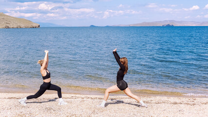 Women practicing yoga on a sunny beach near clear blue water with mountains in the background