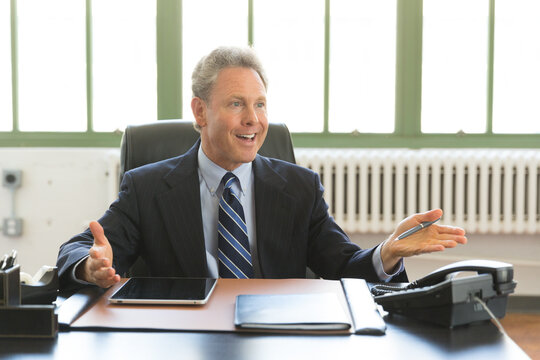 Portrait of busy, Mature Caucasian businessman looking up from work inside office and addressing someone off camera
