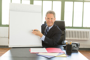 Portrait of busy, Mature Caucasian businessman at a desk pointing to a blank paper flip chart