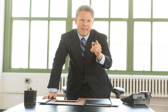 Portrait of busy, Mature Caucasian businessman confidently looking up from work inside office snd pointing at someone,