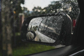 Drops of rain on the window and on the wing mirror, Wet pavement in the background.
