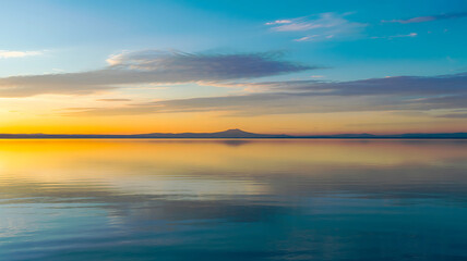 Obraz premium Golden sunset over calm ocean with distant mountain silhouette water