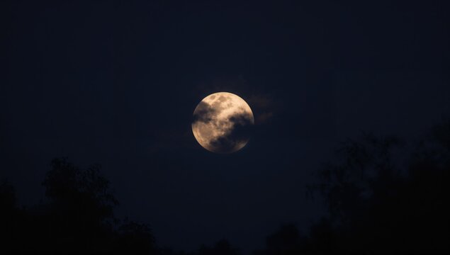 A Full Moon shines brightly in the night sky, illuminating the darkness, celestial event
