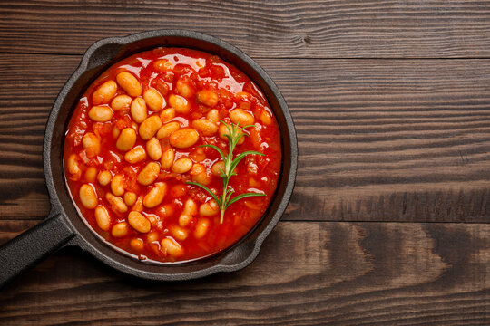 Baked bean dish in cast iron pan on wooden background.	