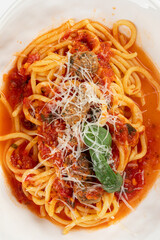 Closeup on cooked pasta topped with tomato sauce meatballs basil and grated cheese on white background