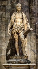 Statue of St Bartholomew inside Duomo di Milano showing detailed anatomical sculpture in dim cathedral interior