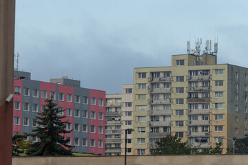 Colorful residential buildings beneath clouds, Vibrant apartment clusters with antennatopped rooftops, Lively collection of multicolored apartment blocks against subdued city skyline backdrop