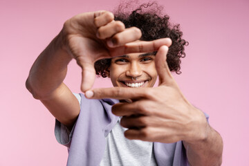 Fototapeta premium Smiling happy Latin man with piercing in nose showing frame with fingers isolated on pink background
