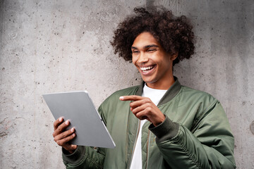 Smiling handsome Latin man holding digital tablet pointing finger looking at camera