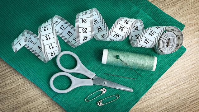 A set of sewing tools on green fabric: scissors, tape measure, thread, pins, and needles. Concept of handcrafting, sewing, creativity, and tailoring. - Powered by Adobe
