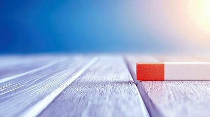 A close-up shot of a red and white rectangular object resting on a light-colored wooden surface, with a soft blue background.