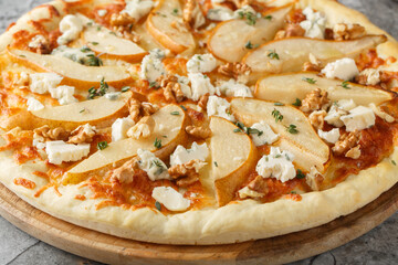 Delicious pizza with pears, gorgonzola cheese, walnuts and herbs closeup on the wooden board on the table. Horizontal