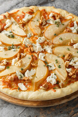 Pizza with pear, blue cheese, walnuts and thyme close-up on a wooden board on the table. Vertical
