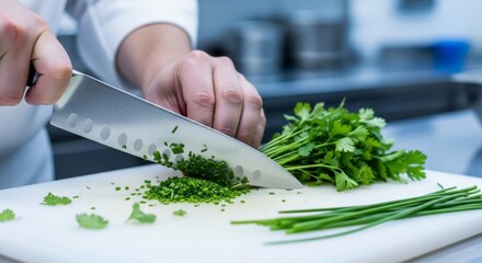 Chef chopping fresh herbs on a white cutting board with a knife.