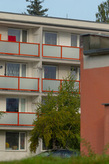 Apartment with balcony, Exterior view of residential building, Residential structure featuring orange railings and lush trees, Balconyequipped dwelling with vibrant rails and landscaped surroundings