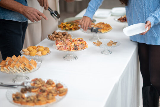 Guests enjoy a delicious spread of appetizers and food at a private event buffet with a selection of savory bites and sweet treats being served and chosen from the beautifully arranged table - Powered by Adobe