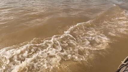 Brown river water churns behind a moving boat, creating foamy waves and turbulence on the surface in Mekong Delta River, Vetnam.