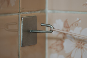 Stainless steel hook attached to a tile with a cord.
