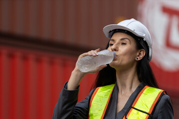 Tired female construction worker in hard hat drinks water from plastic bottle, feeling relief from heat and thirst