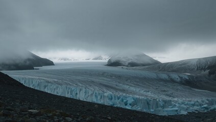 Expansive glacier on rocky hillside enveloped in mist with distant snowy peaks shrouded in rain clouds, erosion risk