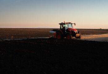 Obraz premium Tractor plowing field the land at sunset