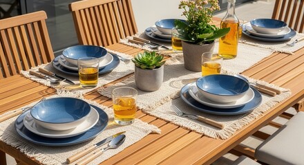 Outdoor wooden dining table set with blue and white dinnerware, clear glasses, cutlery, and potted green plants, ready for a delightful meal.