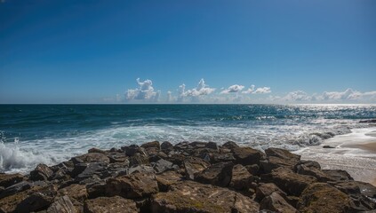 Scenic view of waves crashing against rocky shore with clear sky and ocean