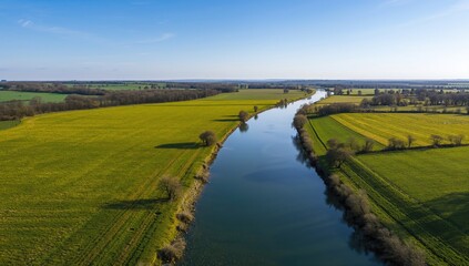 Aerial view of lush green meadows alongside a winding river, showcasing seasonal change