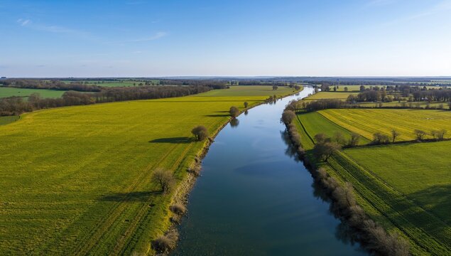 Aerial view of lush green meadows alongside a winding river, showcasing seasonal change