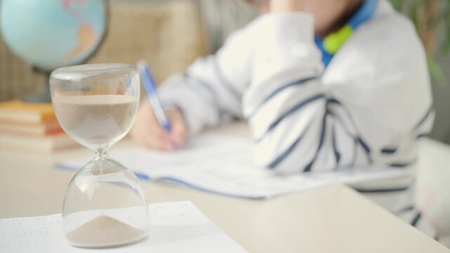 Teenager Student studying doing homework at desk with hourglass, education, knowledge and time management, writing, learning process, exam prep, child training, concentration and discipline sand timer
