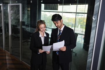 Two business professionals attentively reviewing documents in modern office setting with feeling of collaboration and focus
