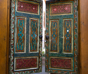 Authentic Double Wooden Doors Partially Open, Featuring Intricate Hand-Carved Traditional Patterns in Vibrant Teal, Burgundy, and Gold Paint Detailing