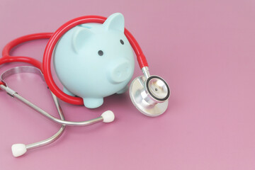 Blue piggy bank and red stethoscope on purple background. Health insurance cost concept. Copy space for text.