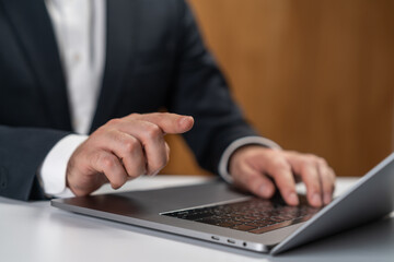 Businessman using laptop with one hand pointing and the other typing, close-up of fingers in corporate setting on blurred office background.