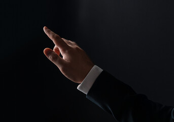 Businessman's hand reaching out with fingers extended against dark background, symbolizing touch,...