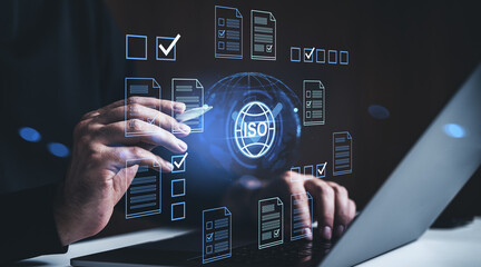 Digital ISO certification concept with holographic documents and checkmarks on a futuristic interface over a person using a laptop in a creative workspace.