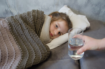 A little girl is lying in bed sick. A glass of water in bed