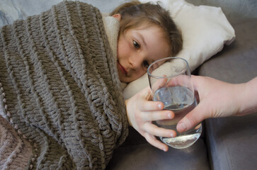 A little girl is lying in bed sick. A glass of water in bed
