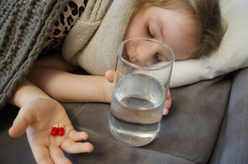 A little girl is lying in bed sick. A glass of water in bed