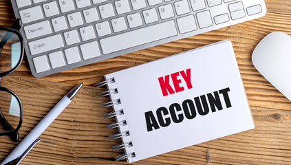 Key account phrase on spiral notebook with keyboard, mouse, pen and eyeglasses on wooden office desk