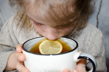 A little girl drinks tea with lemon. Concepts of illness, cold, and acute respiratory viral infection.	