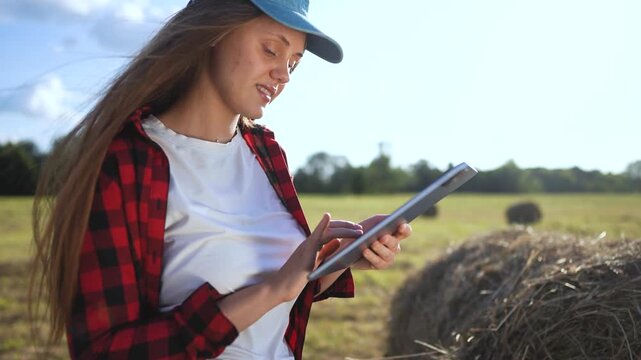 Woman in field holding tablet computer. Girl works on tablet in field. Woman works in a field with haystacks of grass. A woman in a field is holding a tablet lifestyle.
