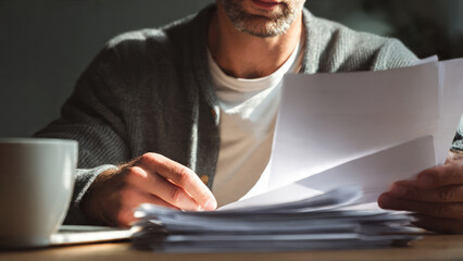 Focused man checking documents over a laptop, hands resting on paperwork. Perfect for business, office workflow, financial review, and productive work moments.